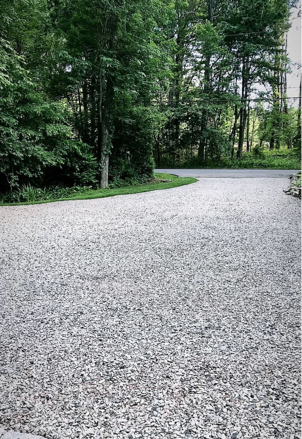 Gravel driveway curving through lush green trees in a serene outdoor setting.