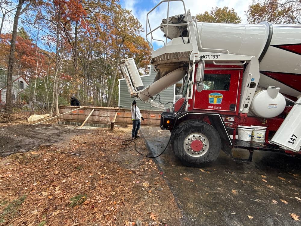 Concrete truck pouring at a construction site surrounded by autumn foliage.