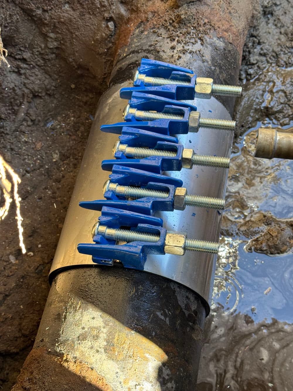 Pipe repair clamp with blue handles attached to a leaking underground pipe.