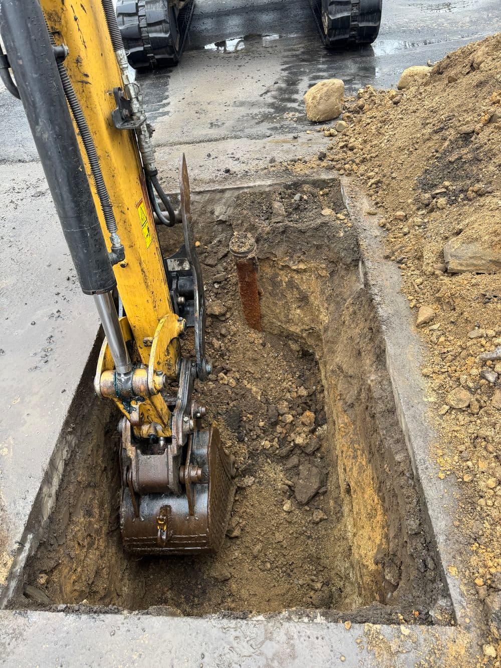 Excavator digging a trench in a construction site with dirt and rocks.