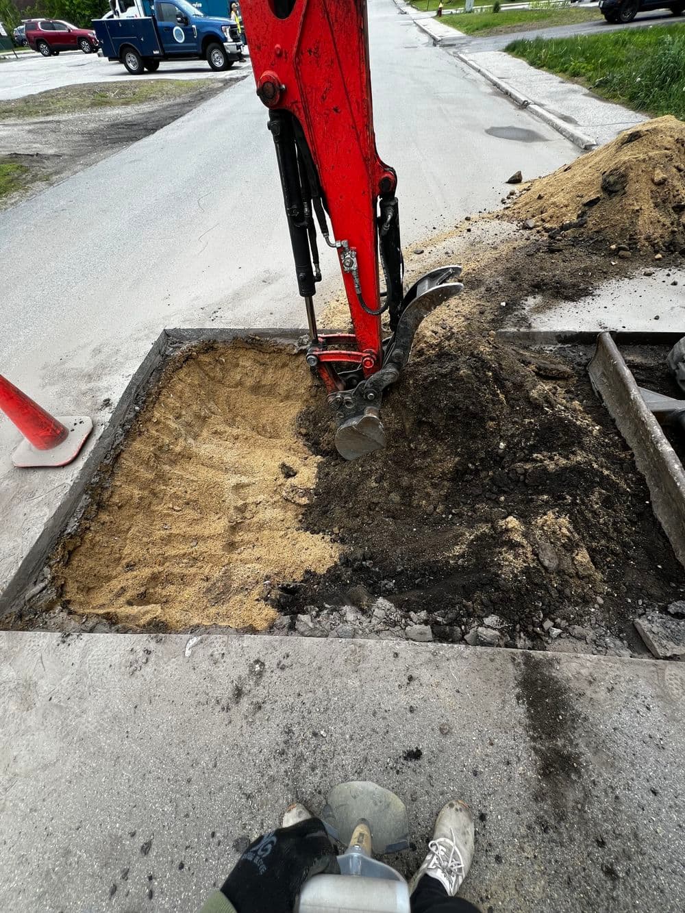 Excavator digging a trench on a city street with surrounding sand and dirt.