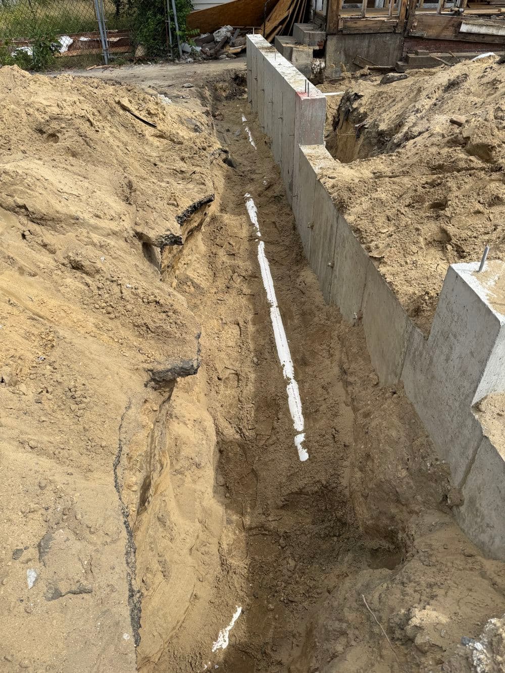 Excavated trench alongside concrete foundation for construction site preparation.