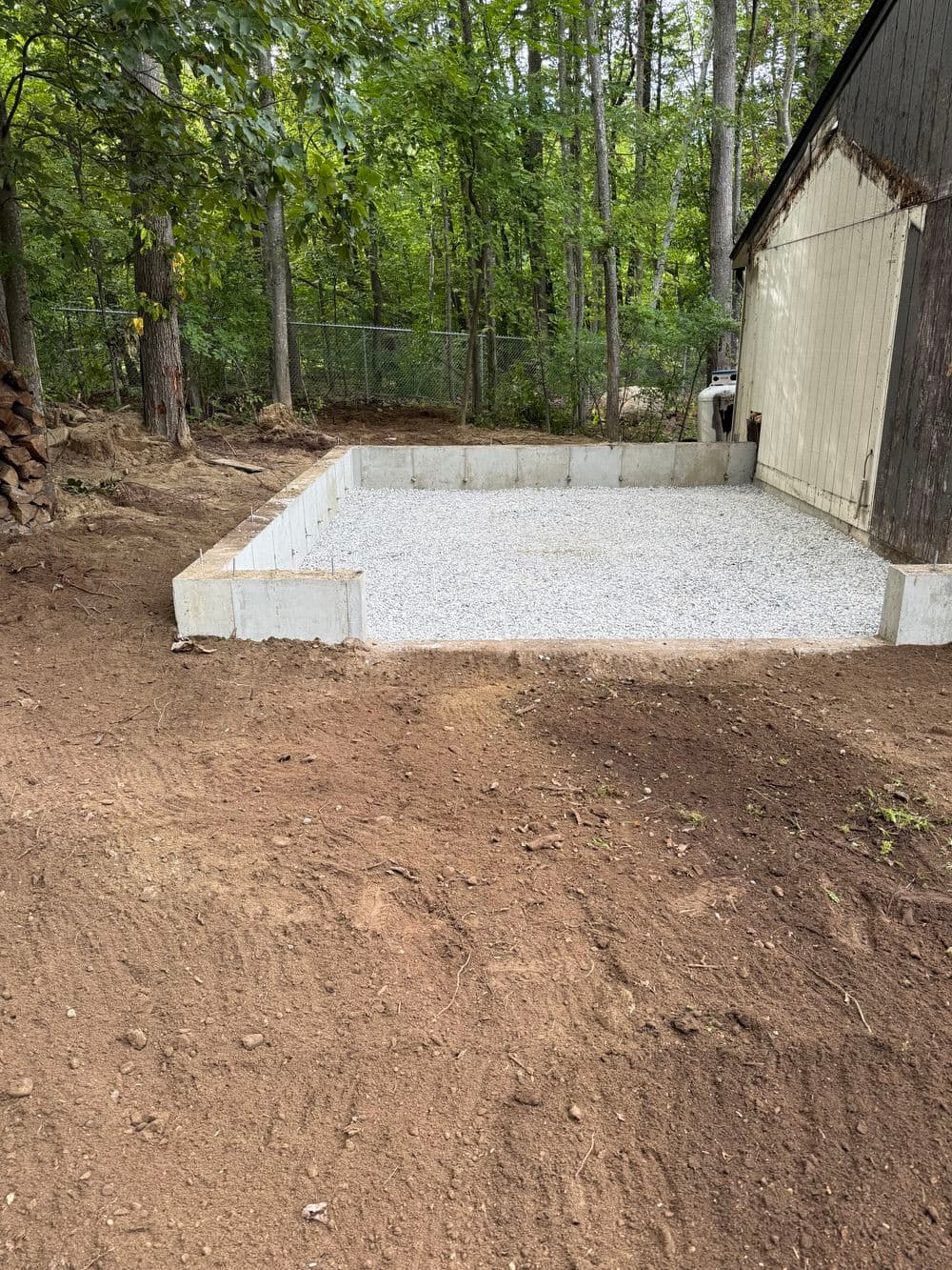 Gravel foundation for a shed surrounded by trees and cleared earth.